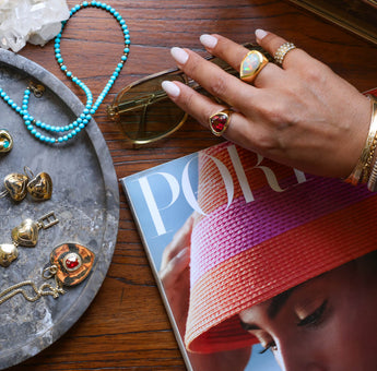 Hand with rings and bracelets above a table with more jewelry