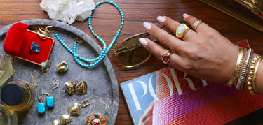Hand with rings and bracelets above a table with more jewelry