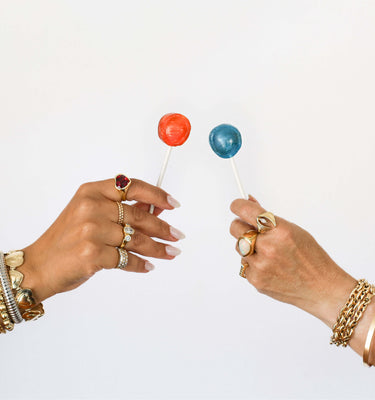 Hands with rings and bracelets cheersing lollipops